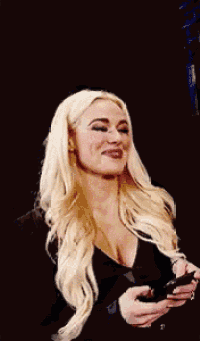 a woman with blonde hair is smiling while holding a cell phone in her hands .
