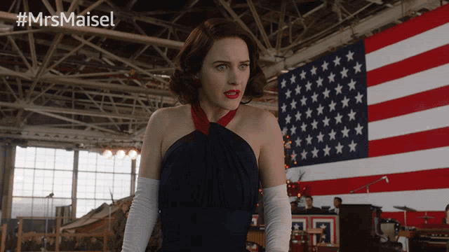 a woman in a blue dress stands in front of an american flag with the hashtag #mrsmaisel