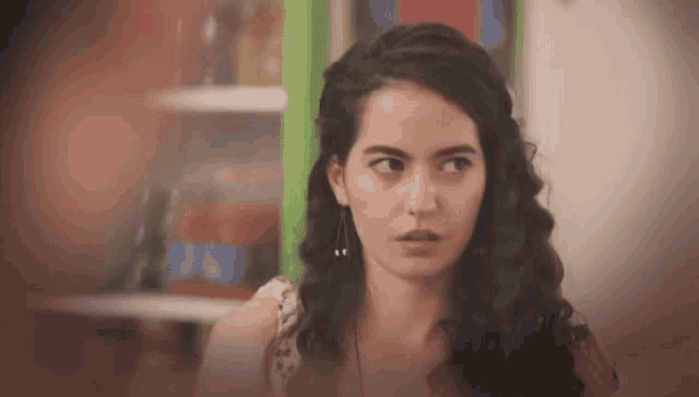 a woman with long curly hair is looking at the camera with a surprised look on her face .