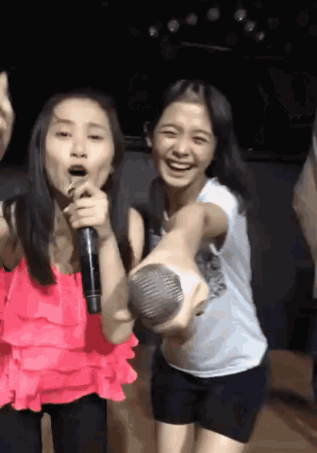 a girl in a pink top is singing into a microphone next to a girl in a white shirt