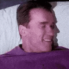 a man in a purple shirt is smiling while laying in bed .