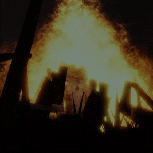 a large fire is burning in the dark with a cross in the foreground