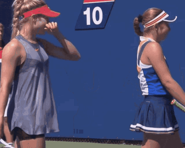 two female tennis players on a blue court with the letter j on the wall behind them