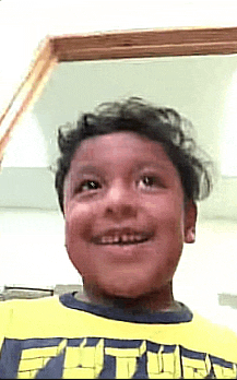 a young boy wearing a yellow t-shirt is smiling in front of a mirror .