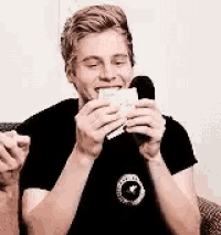 a young man is sitting on a couch eating a sandwich and holding a microphone in his hands .