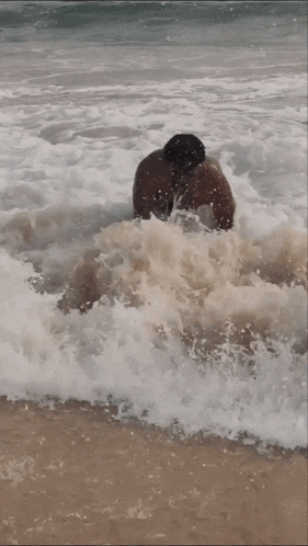 a shirtless man is kneeling in the waves on the beach