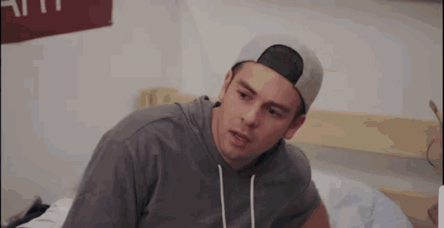 a young man wearing a baseball cap and a gray hoodie is laying on a bed .