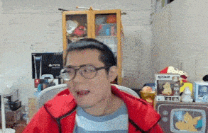 a man wearing glasses and a red jacket is making a funny face while sitting in a chair .