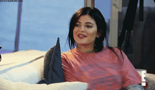a woman in a pink t-shirt is sitting on a bed with her legs crossed .