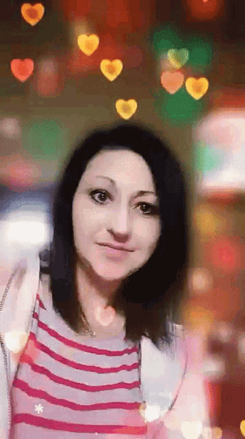 a woman in a striped shirt stands in front of a blurry background of hearts