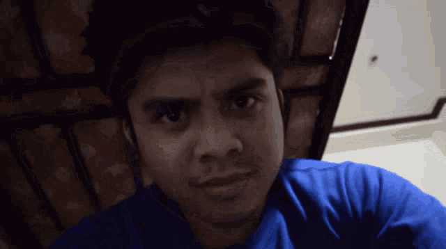 a man in a blue shirt looks at the camera with a serious look on his face
