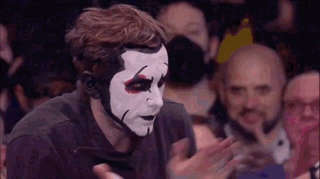 a man with a mask on his face is clapping his hands in a crowd of people .