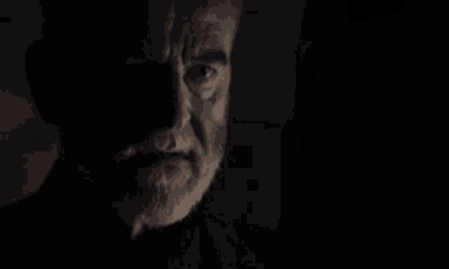 a close up of a man 's face with a beard in the dark .