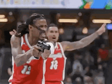 a basketball player is holding a gun in his hand while another player looks on .