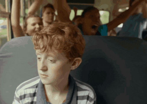 a young boy with red hair sits on a bus