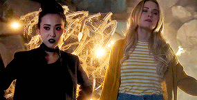 two women are standing next to each other in a dark room . one of the women is wearing a striped shirt .
