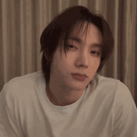 a young man with long hair is wearing a white shirt .