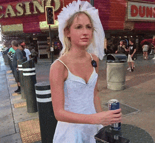 a woman in a wedding dress is holding a can of soda in front of a casino