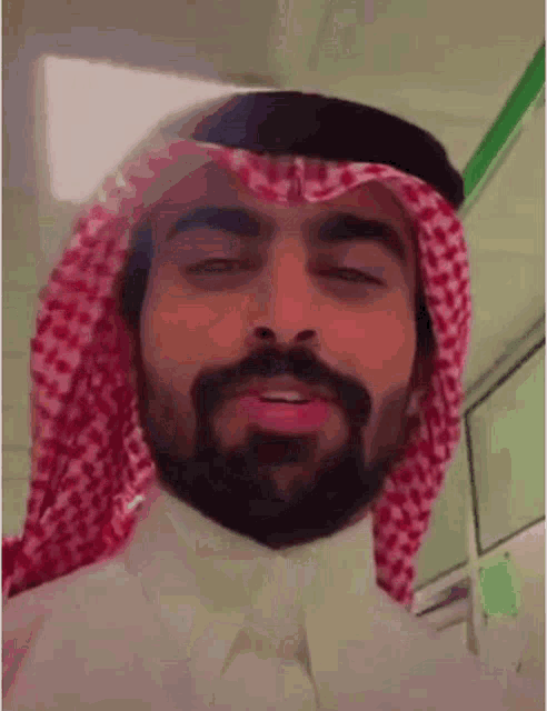 a man with a beard is wearing a red and white checkered scarf around his head .