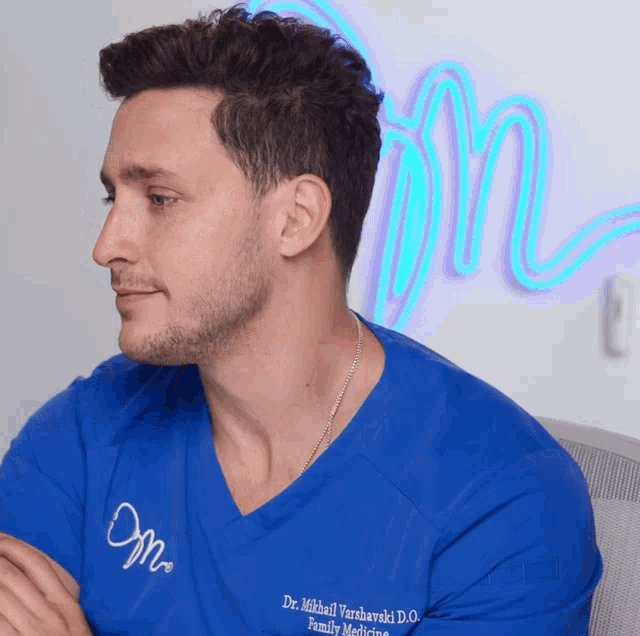 a man wearing a blue shirt that says dr. mikhail varsharski d.o. on it