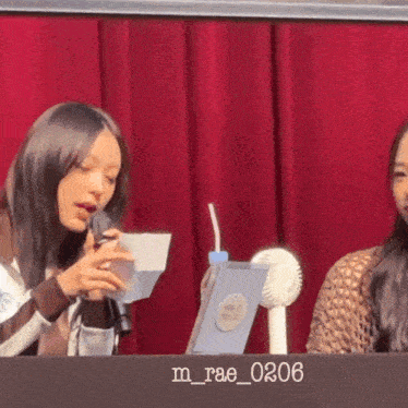 a woman is holding a piece of paper in front of a microphone with the number 0206 on the table