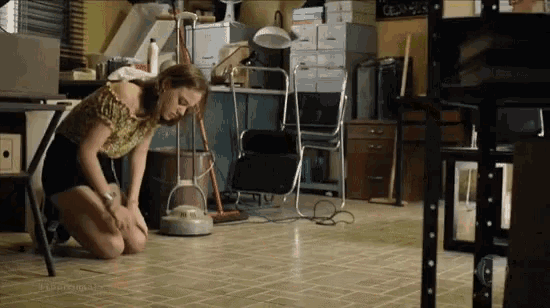a woman is kneeling on the floor in a cluttered room with a vacuum cleaner