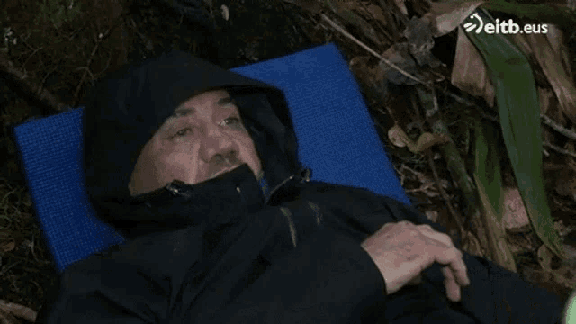 a man in a black jacket is laying on a blue mat with eitb.eus in the background