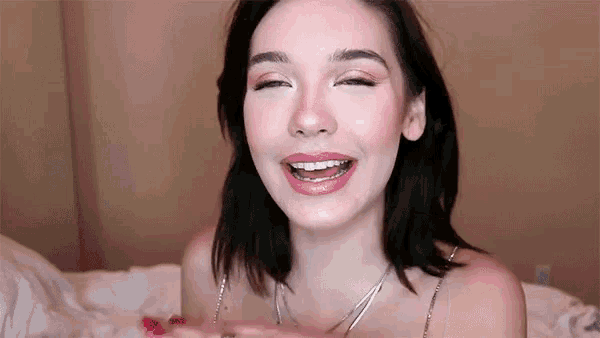 a young woman is laying on a bed with her eyes closed and a smile on her face .