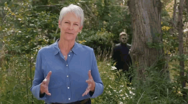 a woman in a blue shirt stands in the woods