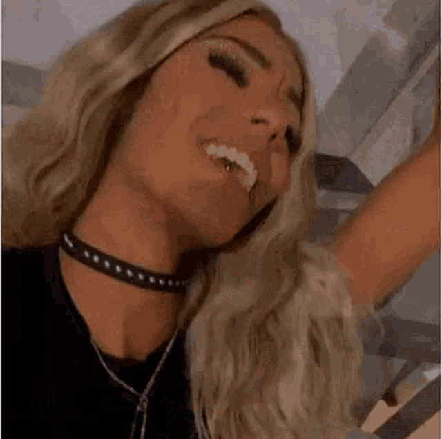 a woman with blonde hair and a nose ring is smiling and pointing at the camera .