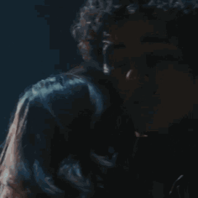 a close up of a man 's face with curly hair in a dark room