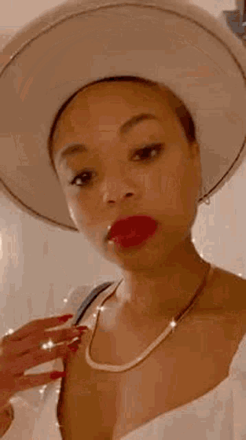 a woman wearing a hat , necklace , and red lipstick is making a face .