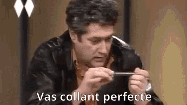 a man in a leather jacket is sitting at a table holding a piece of metal in his hands .