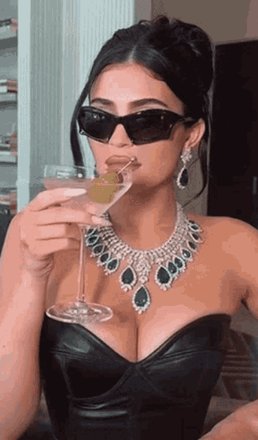a woman wearing sunglasses and a necklace drinking a martini