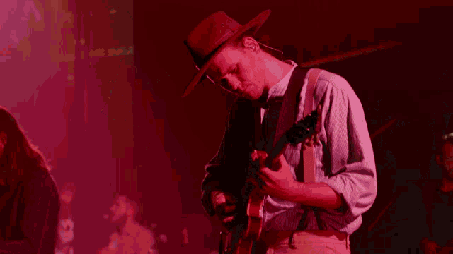 a man in a hat is playing a guitar in a dark room
