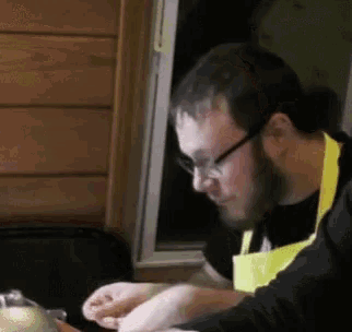 a man wearing glasses and a yellow apron looks down at something