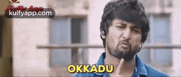 a man with a beard is making a funny face and the word okkadu is on the screen .