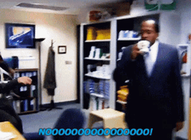 a man in a suit drinking a cup of coffee in an office with the words no 000000 on the bottom