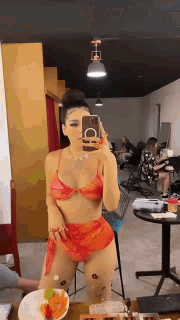 a woman in an orange bikini is taking a picture of herself in a mirror .