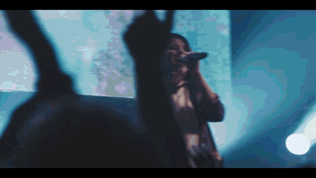 a woman singing into a microphone in front of a crowd with their hands in the air