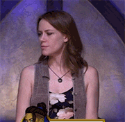 a woman wearing a floral dress and a gray vest is sitting in front of a purple wall .