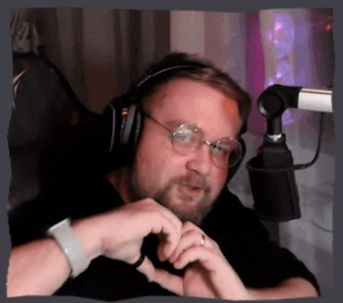 a man wearing headphones and glasses is making a heart shape with his hands in front of a microphone .
