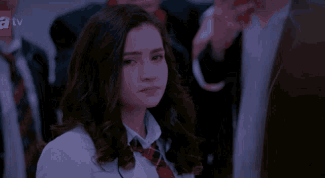 a girl in a school uniform looks at the camera with a tv logo behind her