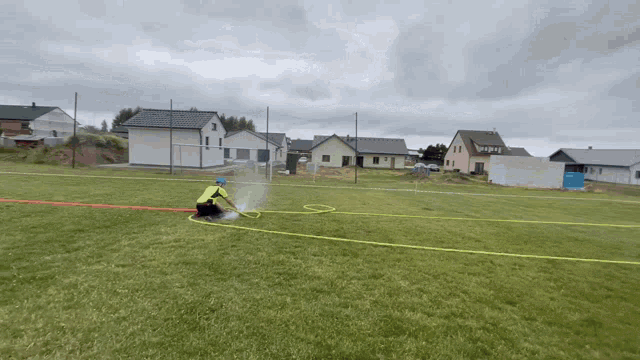 a man in a yellow vest is spraying a hose on a field