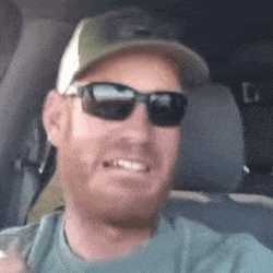 a man wearing sunglasses and a hat is sitting in a car and smiling .