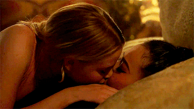 a couple of women kissing on a bed in a room