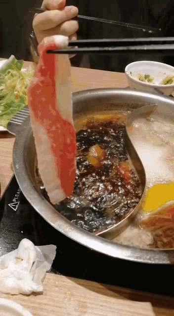 a person is holding chopsticks over a pot of soup