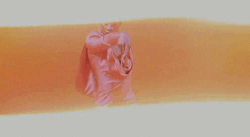 a woman wearing a pink top and earrings is dancing in front of an orange background .