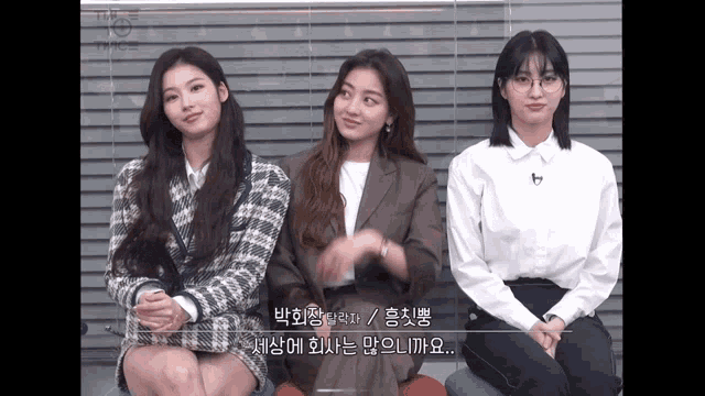 three girls are sitting next to each other and one of them has glasses on