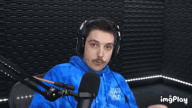 a man wearing headphones and a blue tie dye hoodie is talking into a microphone